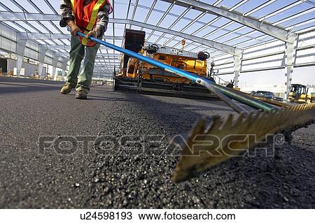 Stock Image - Worker leveling asphalt with a rake; Canada, Ontario, Hamilton (Composting Facility). Fotosearch