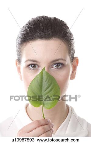 Stock Image - face of a young woman with a leaf held in front of mouth. Fotosearch