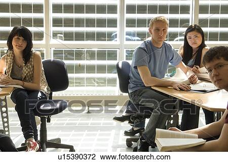 Stock Image - 4 students casually seated at tables in front of solar panelled windows, Winnipeg, Canada. Fotosearch