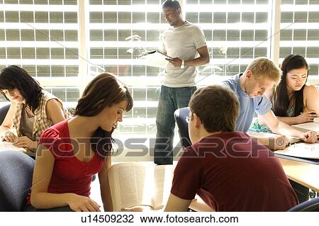 Stock Image - Groups of students casually seated and standing by tables in front of solar panelled windows, Winnipeg, Canada.. Fotosearch