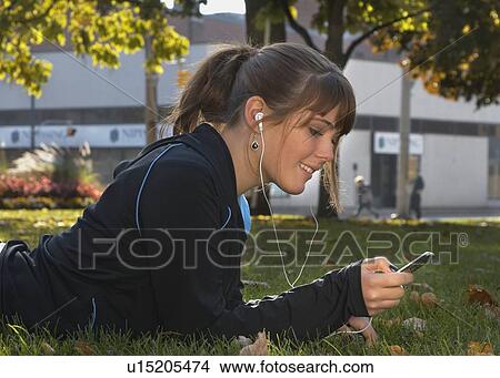 Young woman listening to Ipod outdoors, Brantford, Ontario View Large Photo Image Picture - Young woman listening to Ipod outdoors, Brantford, Ontario. Fotosearch