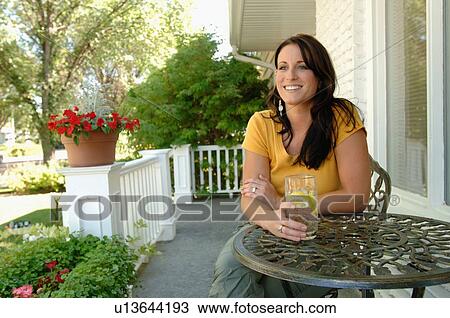 Stock Image - Young woman sitting on porch drinking water, Regina, Saskatchewan. Fotosearch