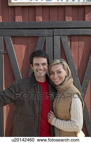 Stock Image - Couple stand beside barn, at organic farm, Ladner, British Columbia, Canada. Fotosearch