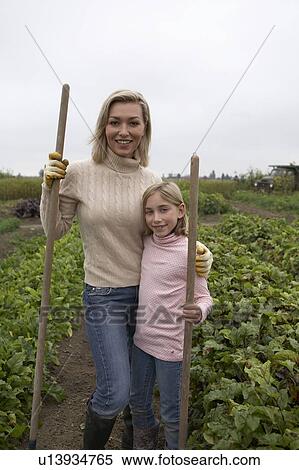 Stock Photography - Mother and daughter posing with gardening tools in organic garden, Ladner, British Columbia, Canada. Fotosearch