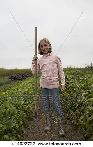Stock Image - Young girl, 9 yrs, holding hoe in organic garden, Ladner, British Columbia, Canada. Fotosearch