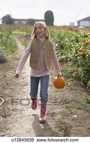 Stock Photo - Young girl standing in field with organic pumpkin, Ladner, British Columbia. Fotosearch