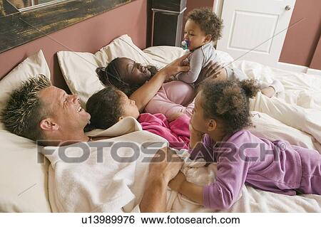 Stock Photograph - AA mom, Caucasian dad, Mulatto Children, Boy 1. 5 years, girl 3 years, girl 6 years. In bed.. Fotosearch