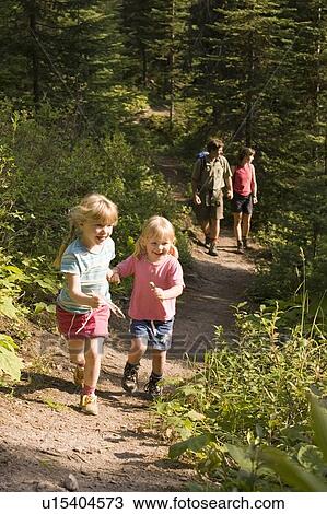 Stock Image - Children run ahead of parents during hike on trail at Island Lake Resort, Fernie, British Columbia, Canada.. Fotosearch