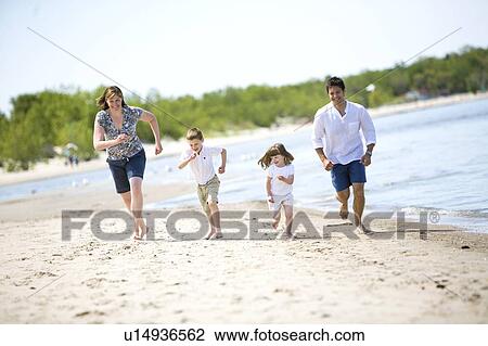 Stock Image - Family of four running along shoreline, Grand Beach Provincial Park, Manitoba, Canada. Fotosearch