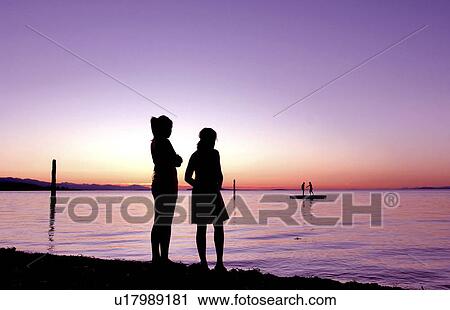 Stock Image - Kids in silhouette against sunset looking over still water. Fotosearch
