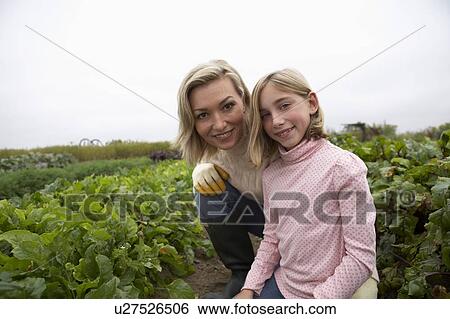 Stock Photograph - Mother and daughter kneeling together in organic garden, Ladner, British Columbia, Canada. Fotosearch