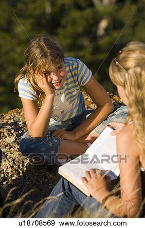 Stock Photo - Two sisters seated outdoors, reading from a book, Saskatchewan. Fotosearch