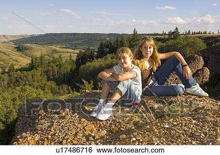 Stock Photograph - Young Sisters (13 and 10) seated outdoors, Saskatchewan. Fotosearch