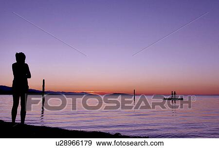 Stock Photo - Kids in silhouette against sunset looking over still water. Fotosearch