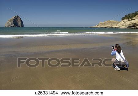 Woman (20-25) photgraphing on a sandy beach with blue sky and rock formations, Newport, Oregon View Large Photo Image Picture - Woman (20-25) photgraphing on a sandy beach with blue sky and rock formations, Newport, Oregon. Fotosearch