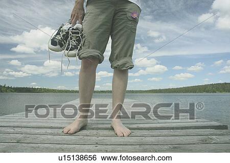 Stock Photograph - Woman standing on dock, Clear Lake; Canada, Manitoba, Riding Mountain National Park. Fotosearch
