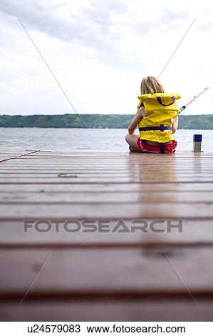 Stock Image - Young girl wearing life preserver fishing off the end of dock at Echo Lake, Saskatchewan, Canada. Fotosearch