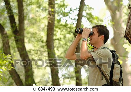 Stock Image - Young man in woods w/binoculars, Regina, Saskatchewan. Fotosearch