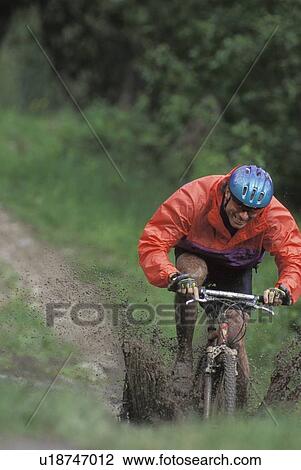 Stock Image - young man mountain biking through mud near Fernie, BC, Canada. Fotosearch