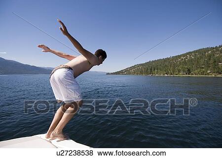 Stock Photo - Youth diving off back of fur-stroke engine boat, Okanagan Centre, BC Canada.. Fotosearch