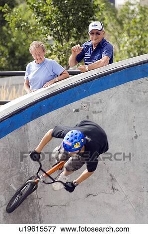 Stock Photo - Senior couple watching a young male riding a bike in a skateboard park, Winnipeg, Canada.. Fotosearch
