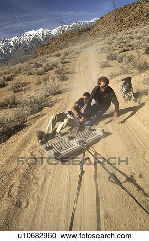 Two men (20-30) surfing behind a car on a plastic palette on a dirt road, Bishop, California, USA View Large Photo Image Stock Image - Two men (20-30) surfing behind a car on a plastic palette on a dirt road, Bishop, California, USA. Fotosearch