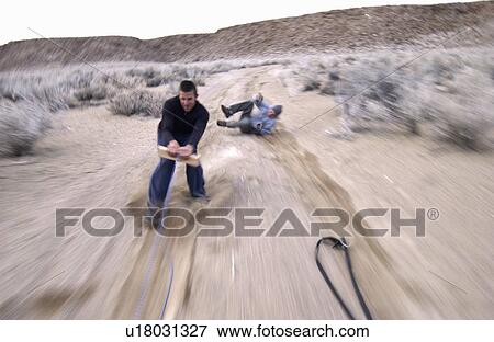 Two men (20-30) surfing behind a car on a dirt road, Bishop, California, USA View Large Photo Image Stock Photo - Two men (20-30) surfing behind a car on a dirt road, Bishop, California, USA. Fotosearch