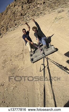 Two men (20-30) surfing behind a car on a plastic palette on a dirt road, Bishop, California, USA View Large Photo Image Stock Photograph - Two men (20-30) surfing behind a car on a plastic palette on a dirt road, Bishop, California, USA. Fotosearch