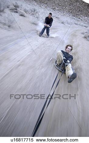 Two men (20-30) surfing behind a car on a dirt road, Bishop, California, USA View Large Photo Image Stock Photography - Two men (20-30) surfing behind a car on a dirt road, Bishop, California, USA. Fotosearch