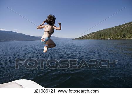 Stock Image - Young woman jumping off back of four-stroke engine boat, Okanagan Centre, BC Canada.. Fotosearch