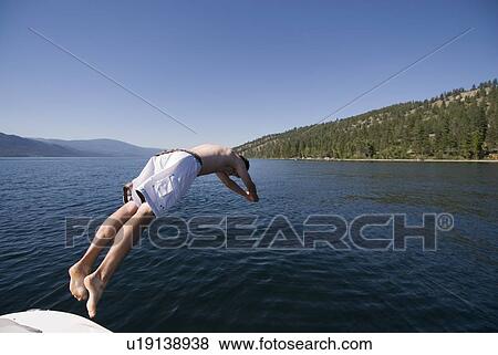 Stock Photo - Youth diving off back of four-stroke engine boat, Okanagan Centre, BC Canada.. Fotosearch