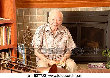 Stock Image - Senior male sitting fireplace; Canada, Saskatchewan, Regina. Fotosearch