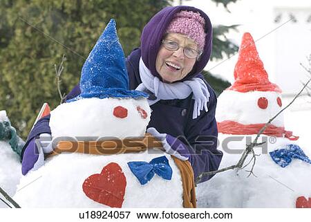 Stock Photo - Senior woman showing off snowman that she made, Winnipeg, Canada. Fotosearch