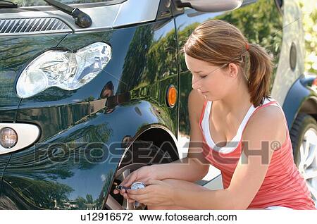 Stock Image - Teenage girl checking tire pressure on smartcar, Regina, Saskatchewan. Fotosearch