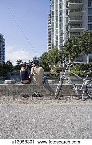 Stock Image - Young Couple rest from riding bikes at a fountain, Vancouver, British Columbia. Fotosearch