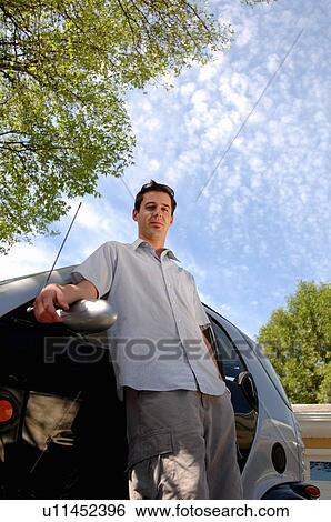 Stock Photograph - Young man leaning against smart car, Regina, Saskatchewan. Fotosearch