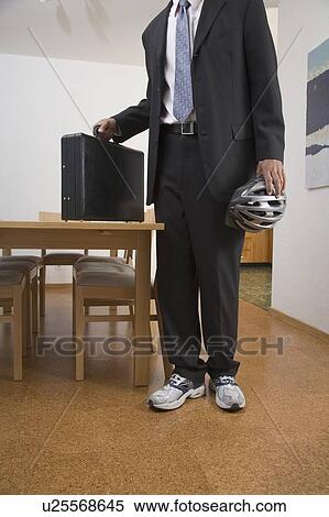 Stock Photography - Young Man on the way to work wearing suit and sneakers holds helmet and briefcase. Fotosearch