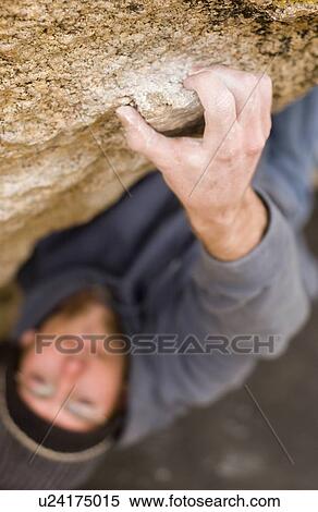 Stock Photography - Man (20-25) clinging to a small handhold while rock climbing, Bishop, California. Fotosearch