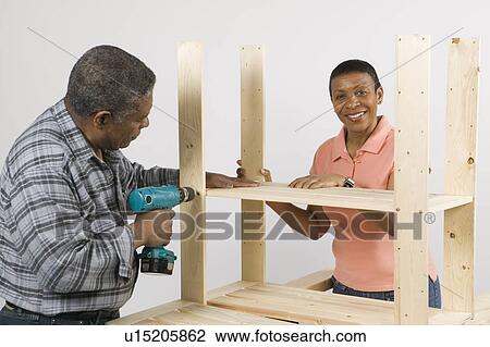 Stock Image - African American Couple Doing Home Improvement, Assembling a Shelving Unit, Canada, British Columbia. Fotosearch