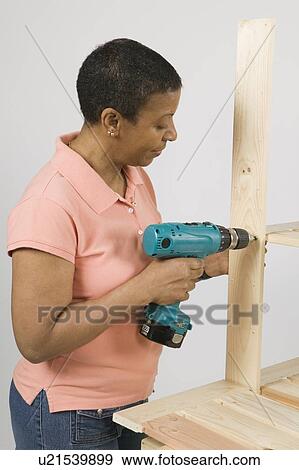 Stock Photo - African American Woman Doing Home Improvement, Assembling a Shelving Unit, Canada, British Columbia. Fotosearch