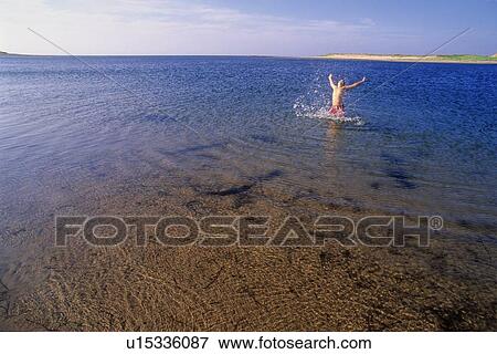 Stock Photo - Boy, 12, jumps out of ocean with arms high, PEI. Fotosearch