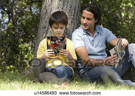 Father and son beside tree reading comic books, Assiniboine Park, Winnipeg, Canada View Large Photo Image Stock Image - Father and son beside tree reading comic books, Assiniboine Park, Winnipeg, Canada. Fotosearch