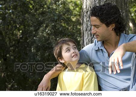 Stock Photo - Father with arm around six year old son beside large tree, Assiniboine Park, Winnipeg, Canada. Fotosearch
