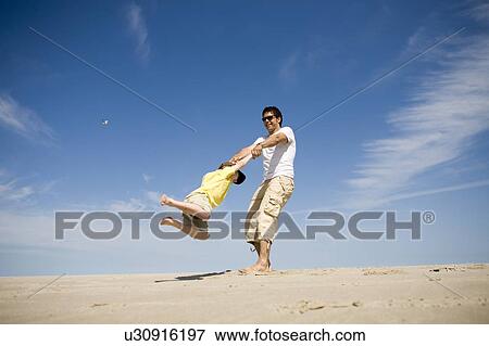 Stock Photo - Man swings boy (7) in circle, Grand Beach Provincial Park, Manitoba, Canada. Fotosearch