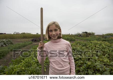 Stock Image - Young girl, 9 yrs, holding hoe in organic garden, Ladner, British Columbia, Canada. Fotosearch
