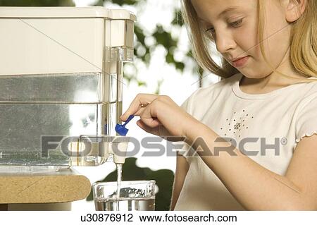 Stock Image - Young girl pouring filtered water. Fotosearch