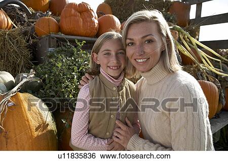 Stock Photograph - Mother and daughter beside hay rack of organic pumpkins, British Columbia, Canada. Fotosearch