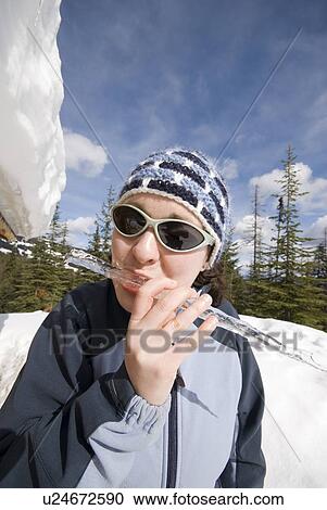 Stock Image - A woman grabs an icicle from the roof of a winter cabin, Silver Star ski resort near Vernon, BC, Canada. Fotosearch