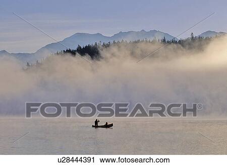 Stock Image - Canoeist on Alta Lake, with mountains and mist. Fotosearch