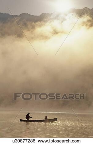 Stock Photograph - Canoeist on Alta Lake, with mountains and mist, Whistler, BC Canada. Fotosearch